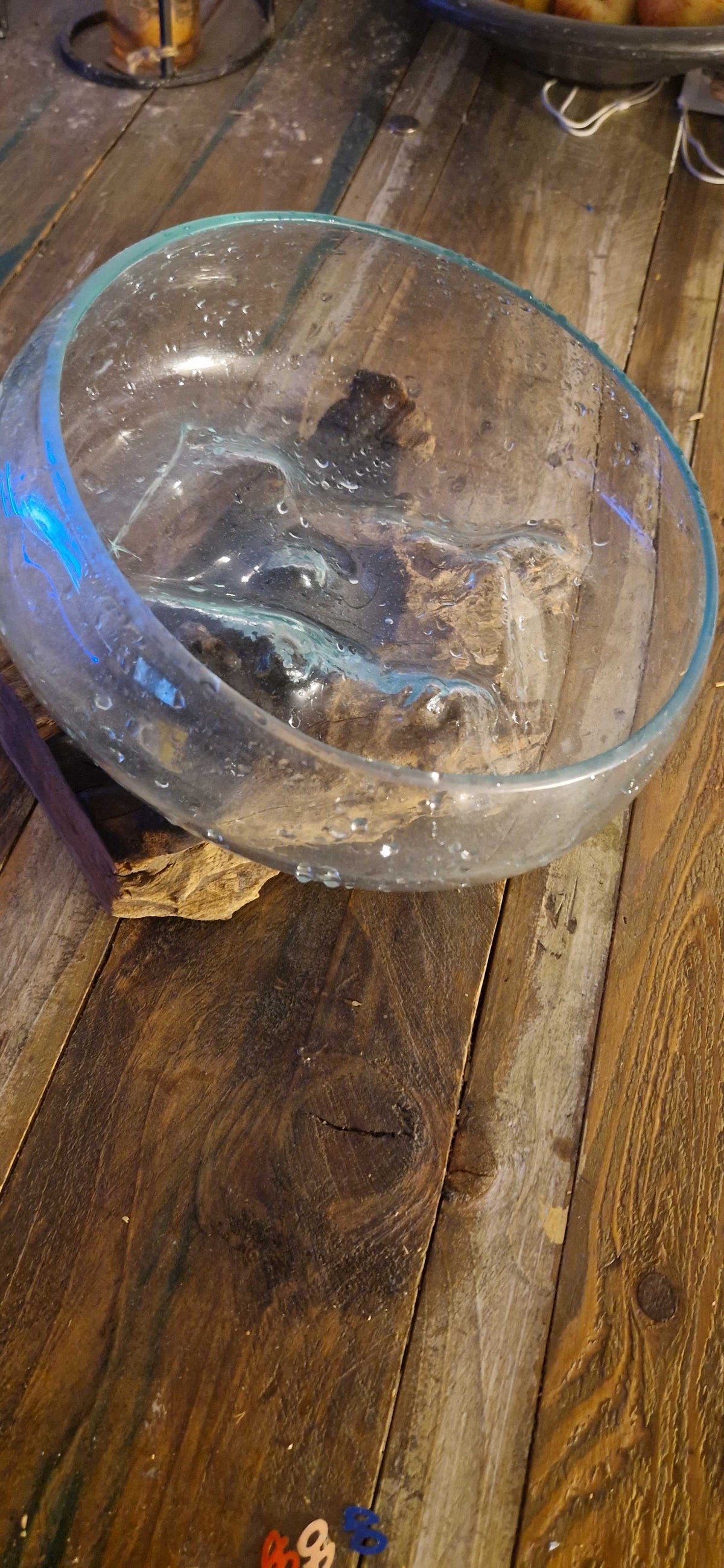 A clear glass bowl with a thick, rounded base and a slightly flared rim, resting on a rustic dark wood plank surface.